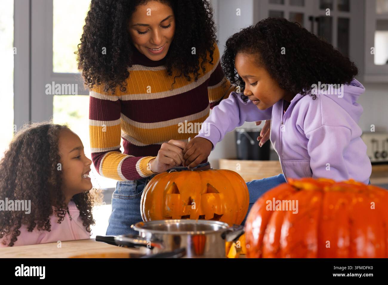 Famiglia afroamericana con ragazzi adolescenti che intagliano una zucca di Halloween in cucina con attrezzi Foto Stock