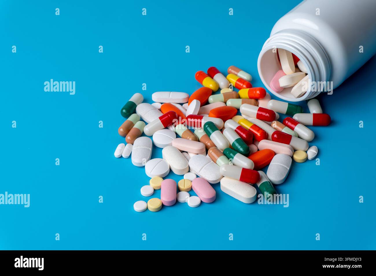 Compresse e capsule mediche colorate che si riversano da una bottiglia di plastica bianca. Sanità, farmacia, farmaci, industria farmaceutica, concetto di trattamento Foto Stock