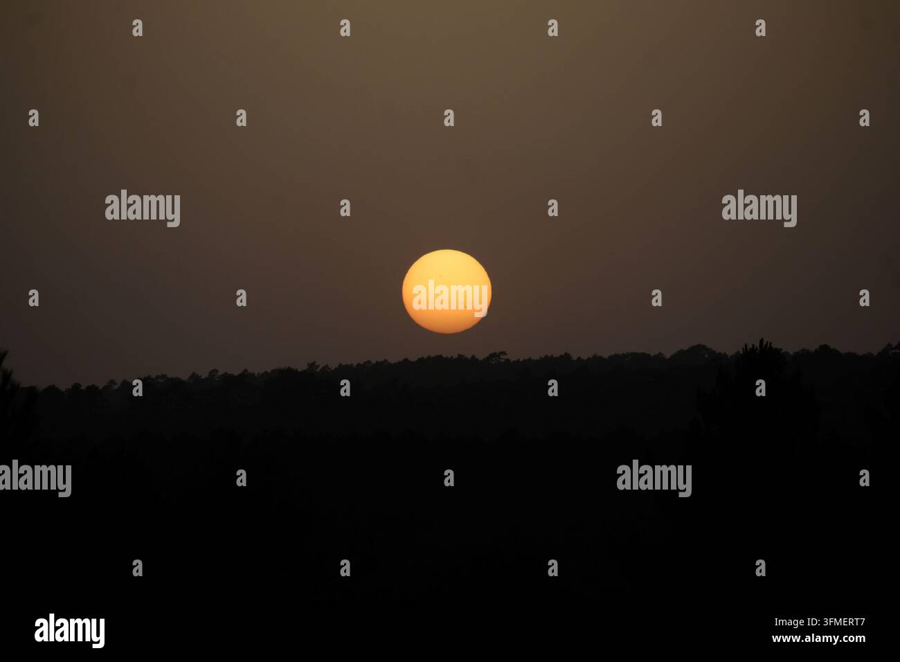 Fotografia del sole brillante nel cielo crepuscolare sopra l'orizzonte montuoso al tramonto. Foto Stock