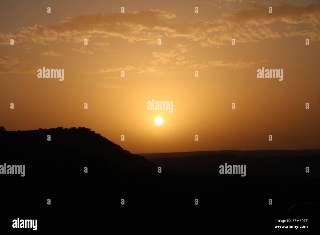 Fotografia del sole brillante nel cielo crepuscolare sopra l'orizzonte montuoso al tramonto. Foto Stock