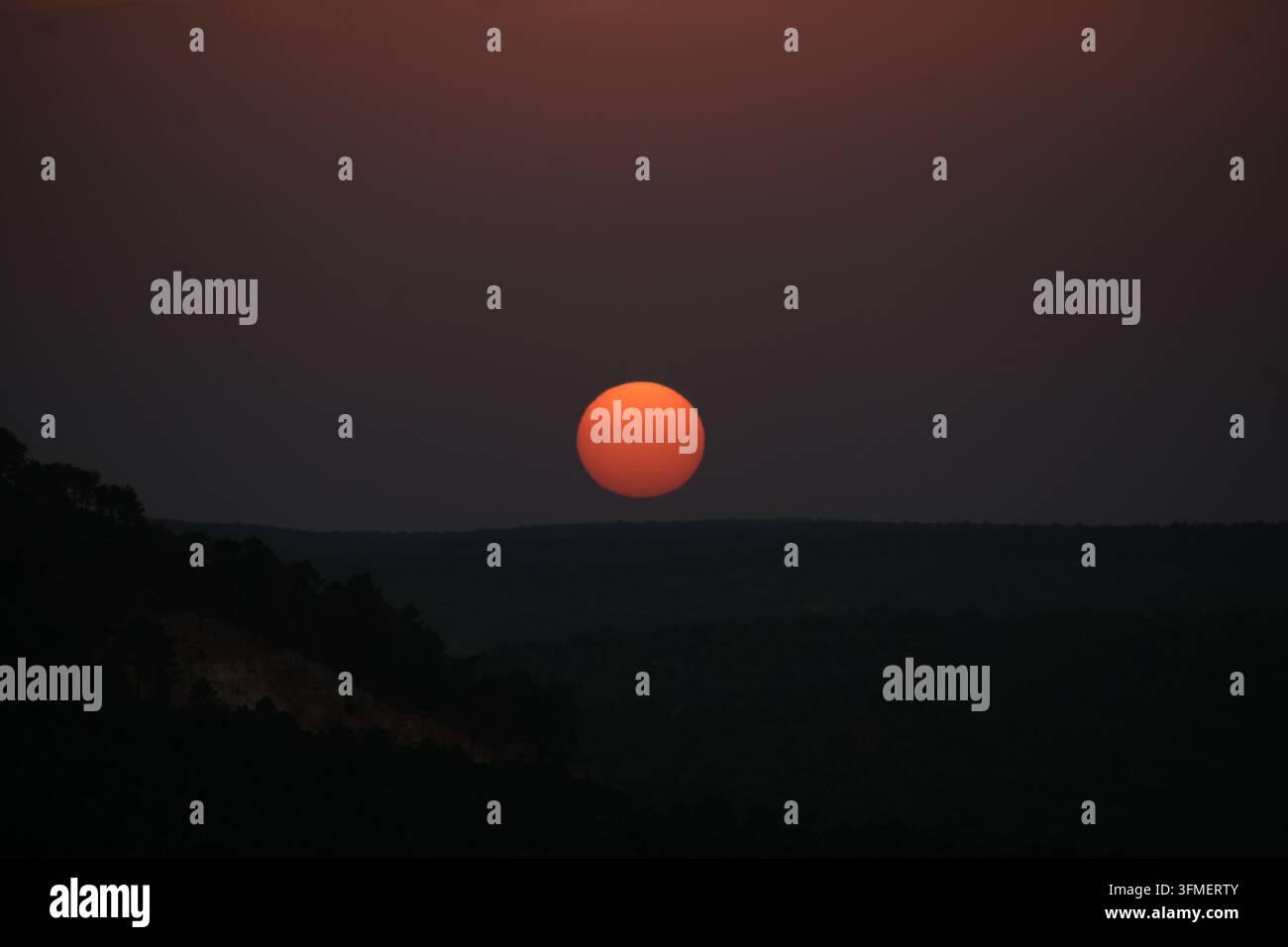 Fotografia del disco solare rotondo posato sull'orizzonte montuoso al tramonto. Foto Stock