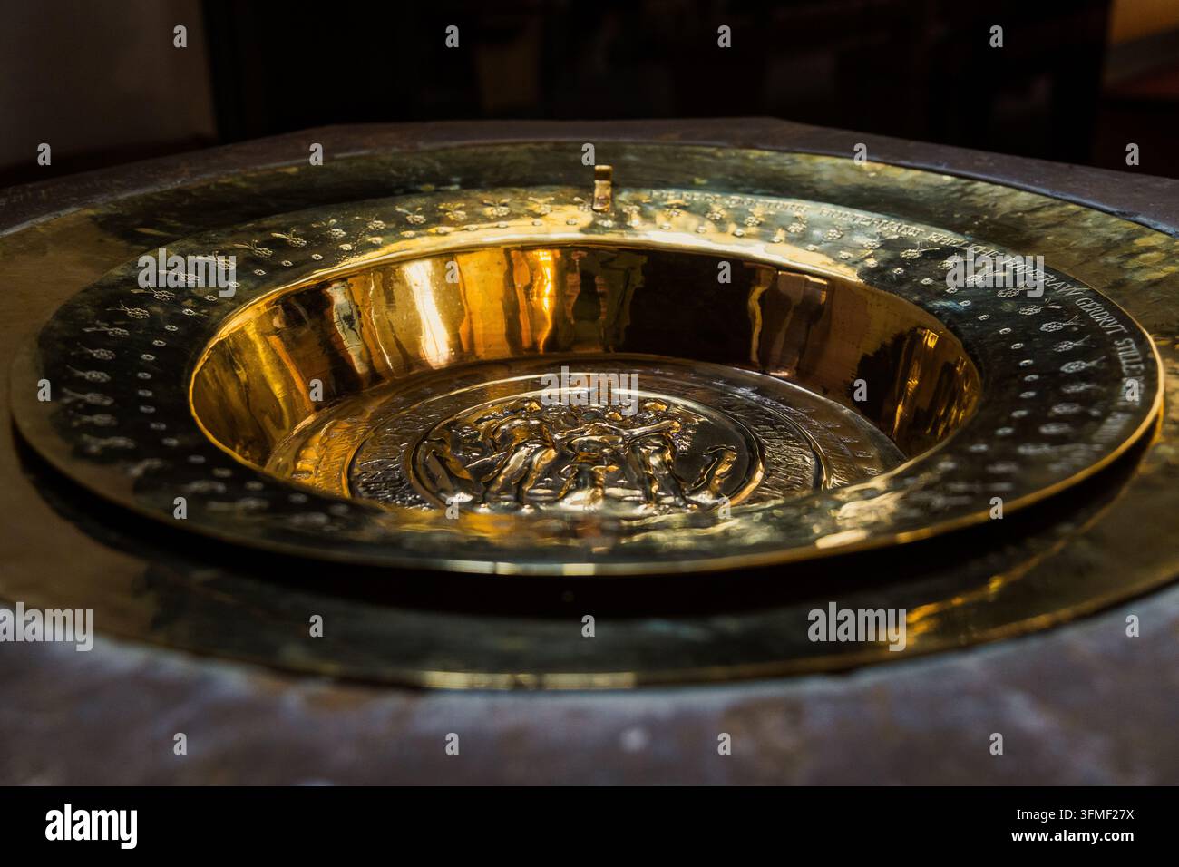 Antico fonte battesimale ornato con bacino in ottone inciso all'interno di una chiesa storica Foto Stock