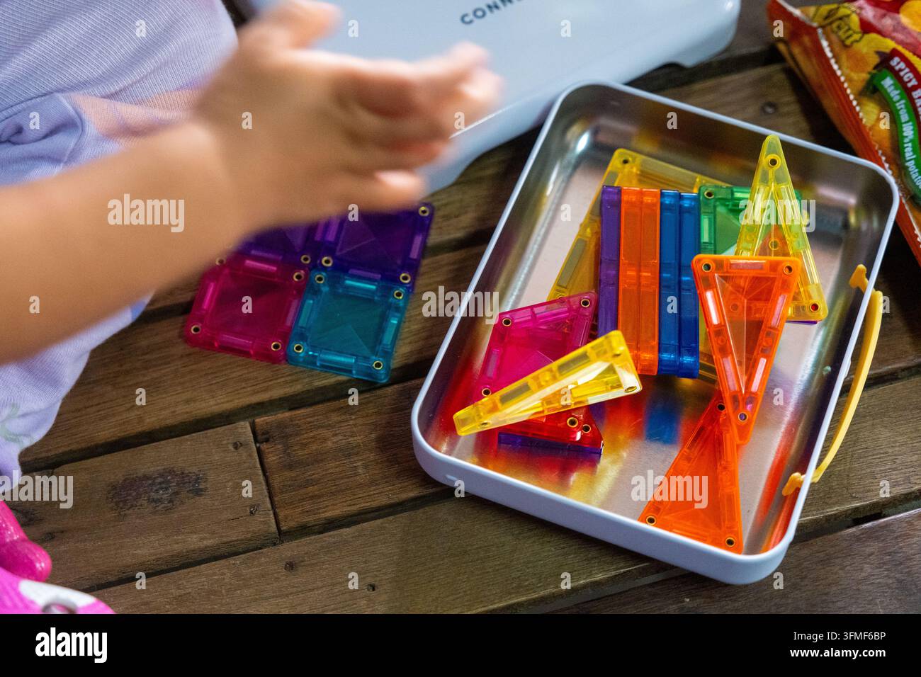 Bambino che gioca con blocchi di costruzione geometrici colorati su un tavolo di legno durante il giorno Foto Stock