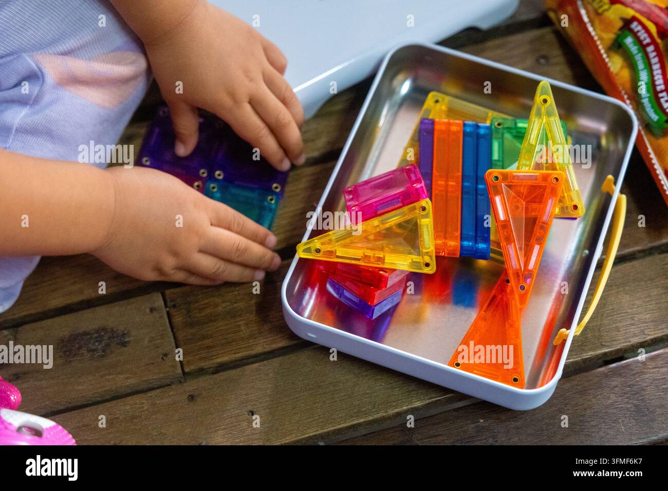 Bambino che gioca con blocchi di costruzione geometrici colorati su un tavolo di legno durante il giorno Foto Stock