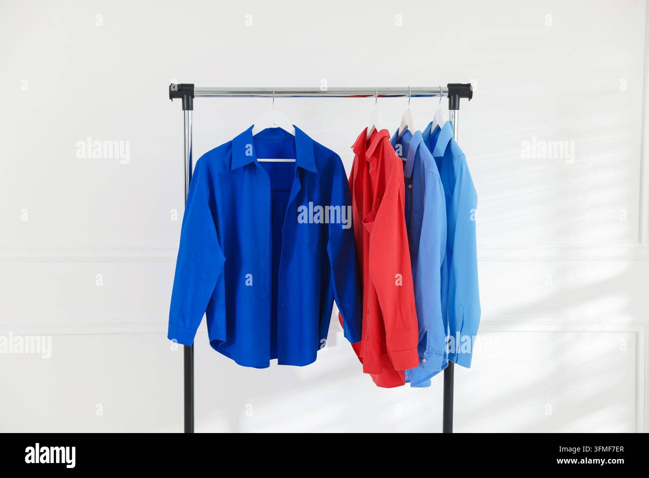 Diverse camicie appese a una rastrelliera vicino a un muro bianco all'interno Foto Stock