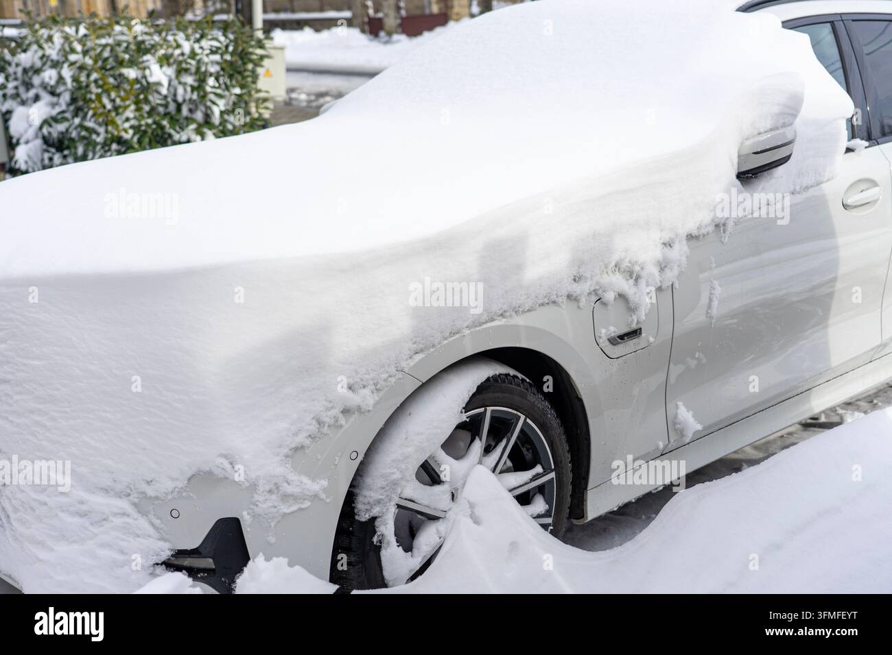 Auto ibrida plug-in coperta di neve parcheggiata all'aperto dopo una forte nevicata. Foto Stock