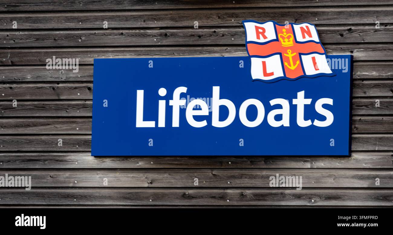 Insegna della Royal National Lifeboat Institution con logo della bandiera RNLI montata su un muro di legno stagionato Foto Stock