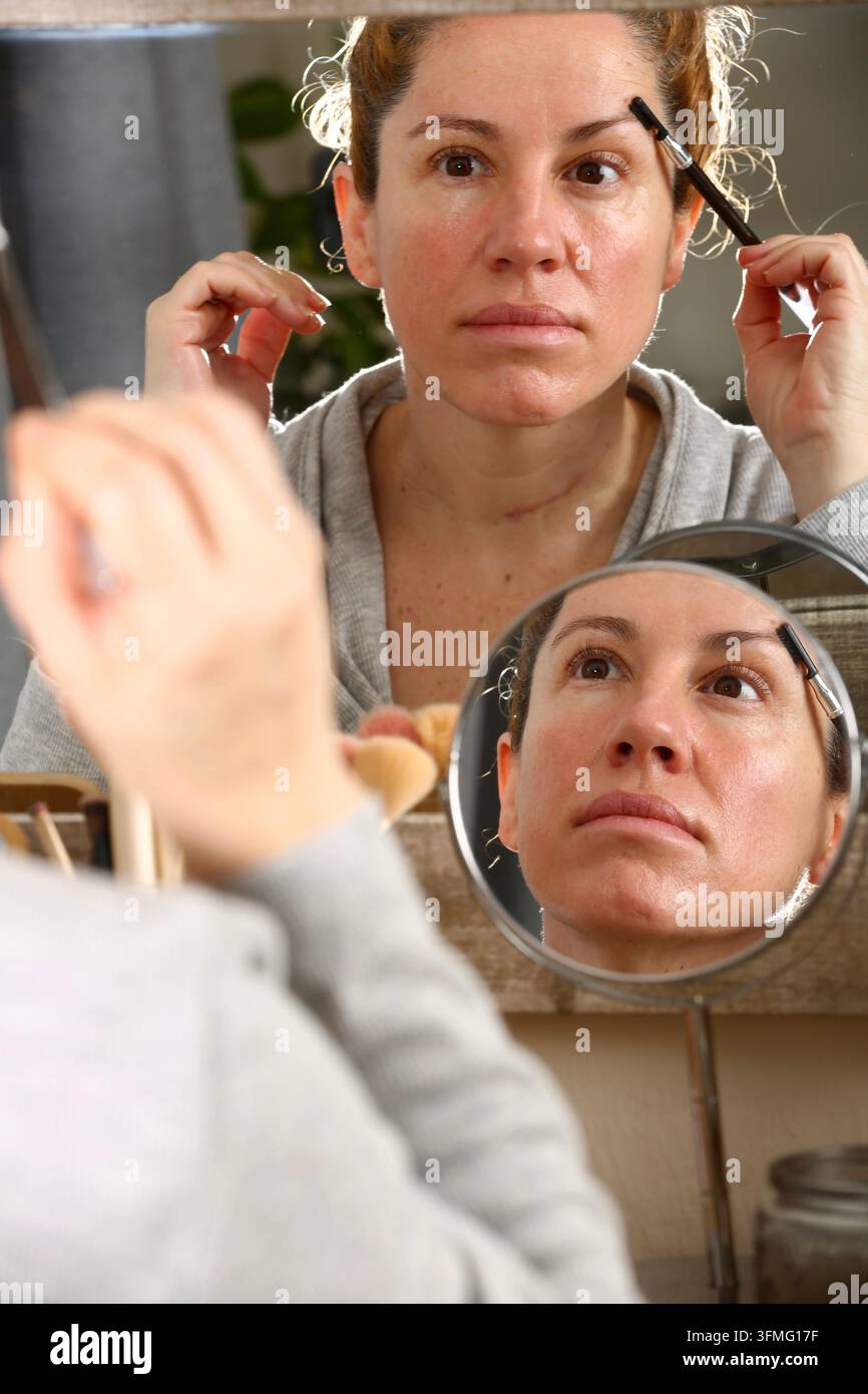 Donna bionda di mezza età con capelli ricci che si trucca davanti a uno specchio Foto Stock