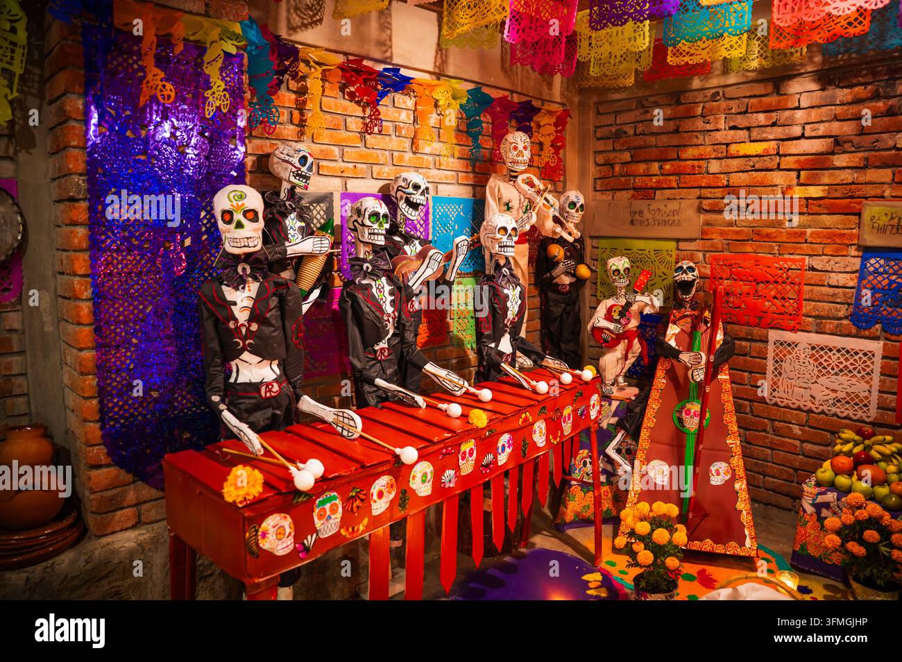 Un gruppo di figure scheletriche artigianali vestite da mariachi suona una marimba rossa e chitarre circondate da fiori di calendula e colorato papel pi Foto Stock