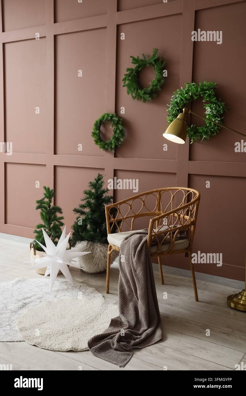 Interno di casa natalizia, stagione delle feste, comfort e decorazione festiva del soggiorno con sedia in rattan, ghirlande di pino e illuminazione calda in un appartamento accogliente Foto Stock