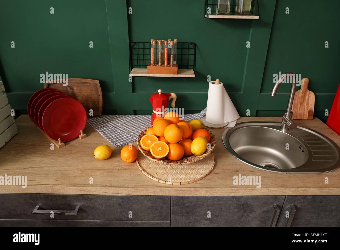 Nutrizione sana e cucina casalinga, arance e limoni freschi in una ciotola su un piano di lavoro moderno della cucina con una moka rossa e uno sfondo murale verde Foto Stock