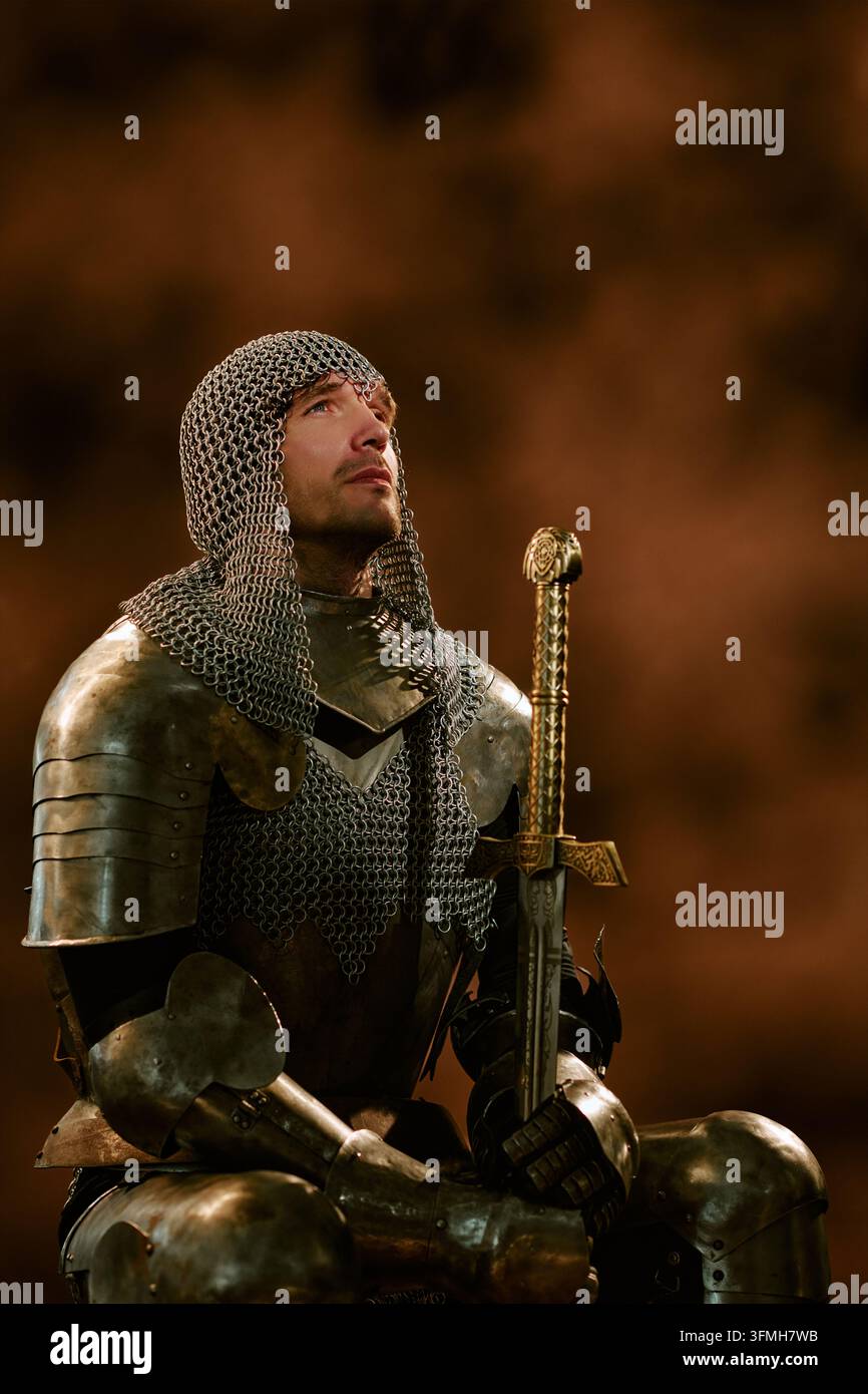 Cavaliere medievale in armatura che tiene una spada e guarda verso l'alto Foto Stock