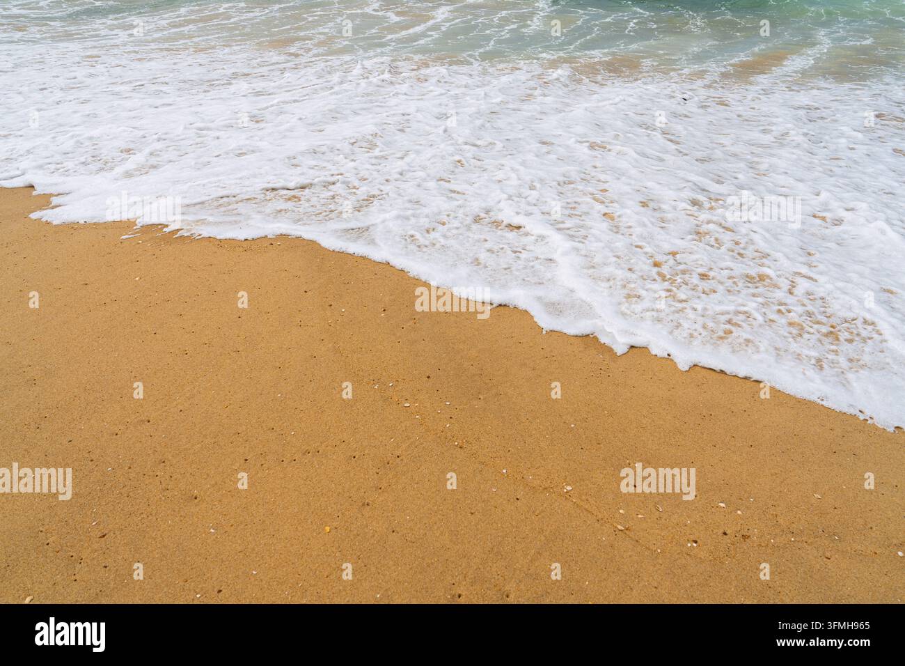 Vista ad angolo alto delle dolci onde dell'oceano che si infrangono su una sabbia dorata di una spiaggia francese soleggiata, catturando il ritmo pacifico della marea e la serenità, luminosa Foto Stock