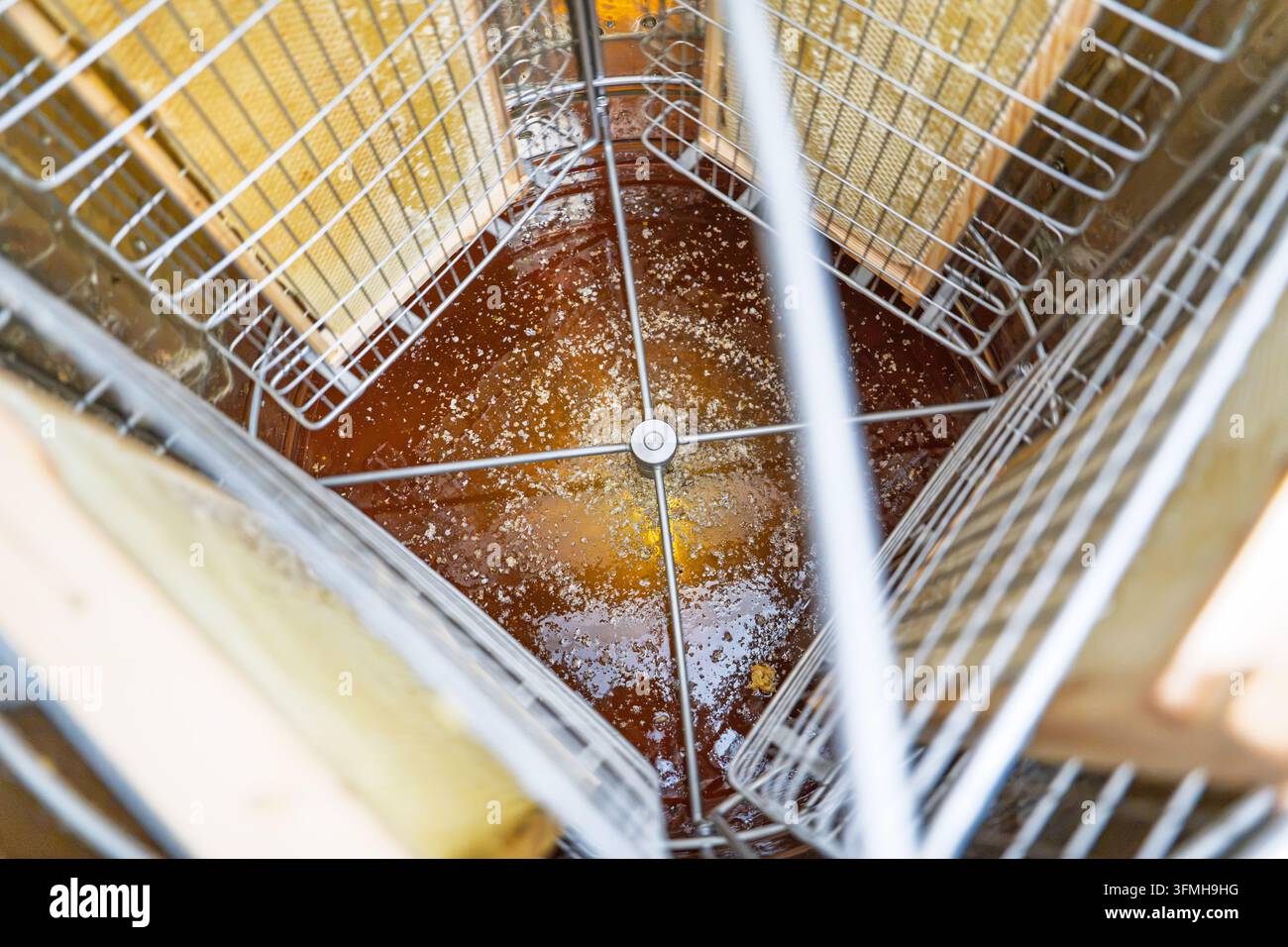 Vista dall'alto di un estrattore di miele in acciaio inossidabile caricato con telai di legno e miele dorato fresco durante l'estrazione manuale con centrifuga in un'apicoltura rurale Foto Stock