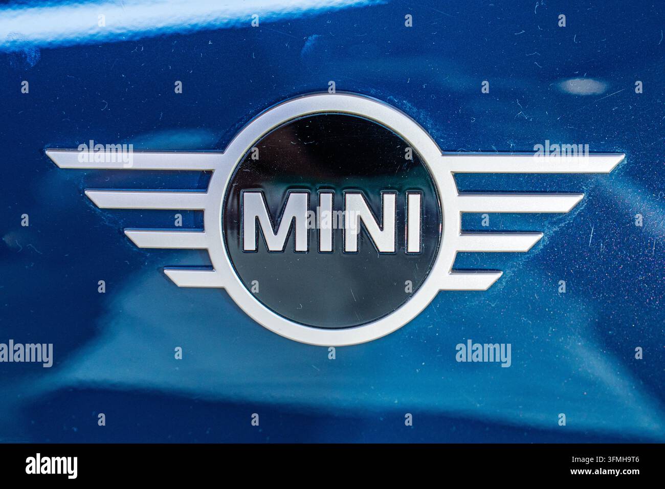 Monaco di Baviera, Germania, 16.07.2024 - Un'immagine macro a distanza ravvicinata che mostra l'emblema argentato e nero Mini Cooper su un pannello blu riflettente dell'auto, enfatizzando l'artigianalità Foto Stock
