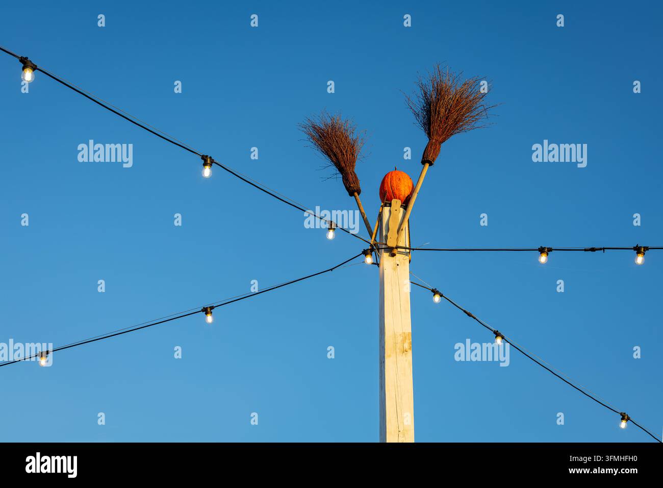 Decorazione rustica per Halloween con testa di zucca e due scope su palo di legno, luci a filo luminose che attraversano un cielo blu sereno della sera Foto Stock