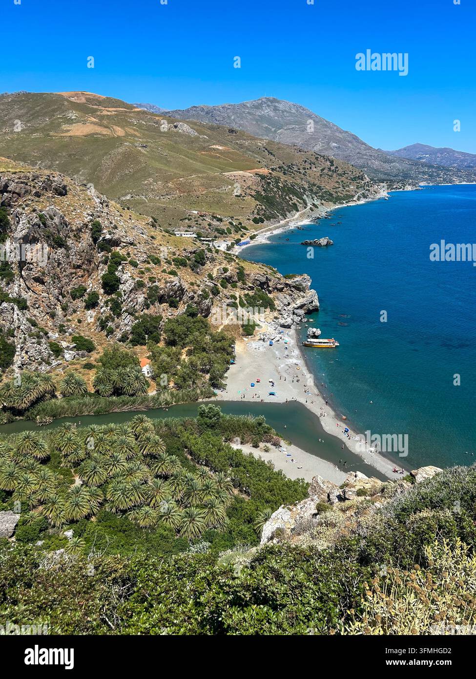Vista ad angolo alto di Preveli Beach a Creta, Grecia, con una foresta di palme, l'imboccatura di un fiume, persone che prendono il sole e il profondo mare libico blu sotto un cielo sereno. - Immagine stock catturata con smartphone