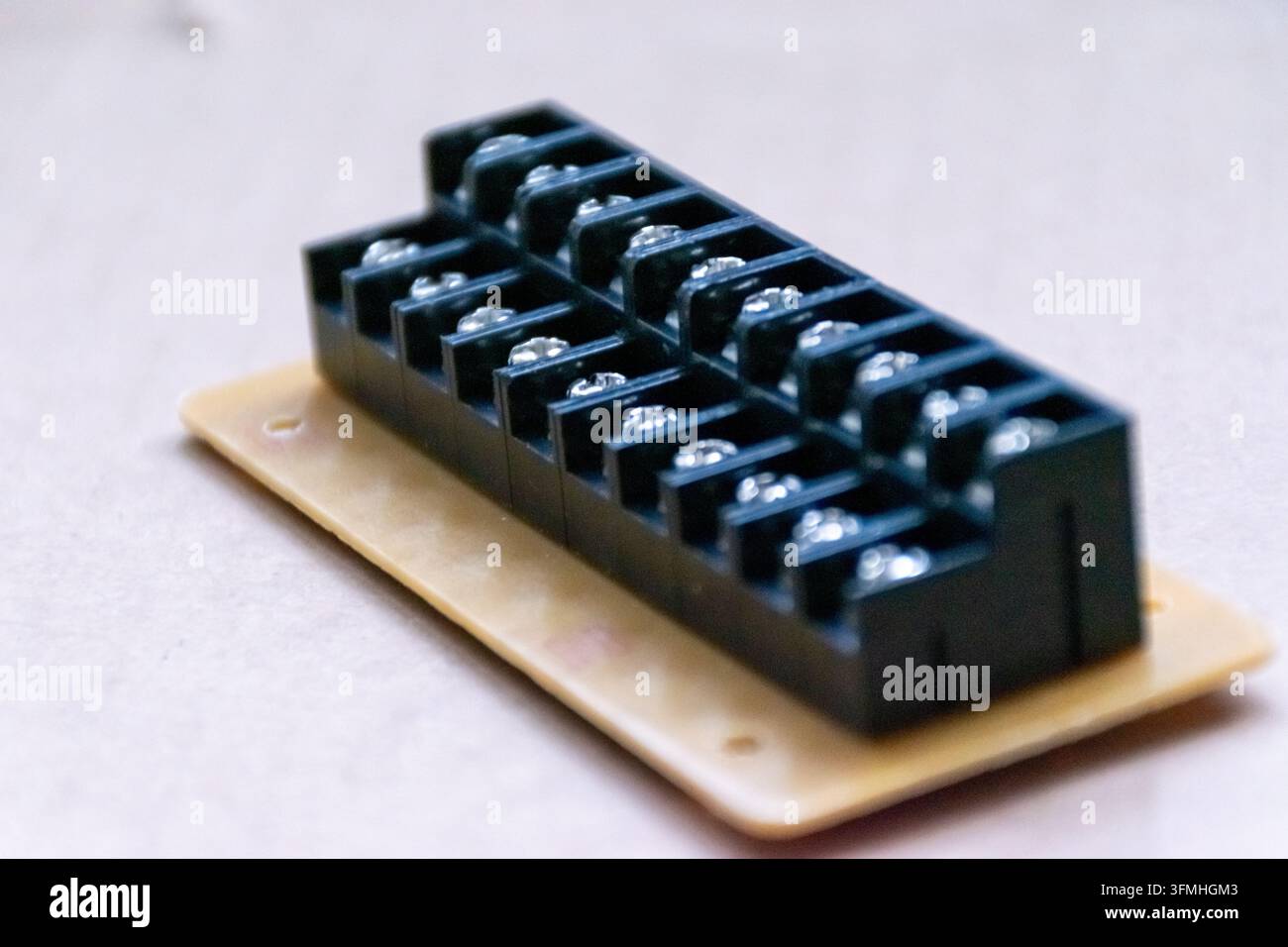 Un blocco di terminali elettrico nero con file di contatti a vite in metallo è posizionato su una piastra di montaggio beige Foto Stock