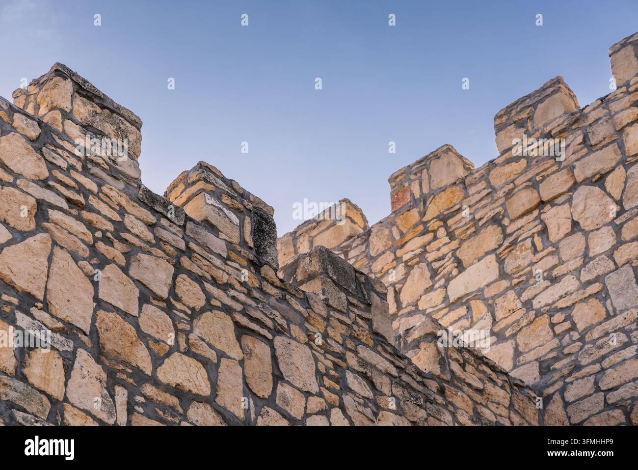 Vista ad angolazione bassa delle merlature di una fortezza in pietra medievale contro un cielo blu limpido Foto Stock