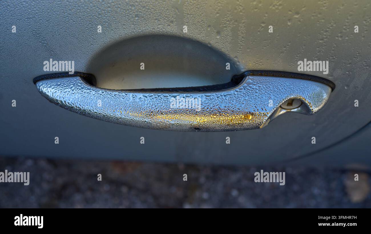 Maniglia della portiera dell'auto coperta di ghiaccio. Il freddo mattutino visibile sulla superficie metallica. I cristalli di ghiaccio luccicano sotto una luce soffusa. Perfetto per temi invernali o di viaggio Foto Stock