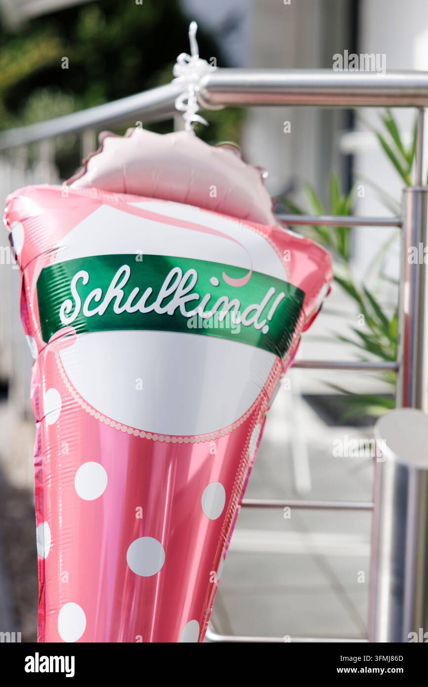Un palloncino rosa con pallini bianchi e uno striscione verde con scritto « Schulkind! » è appeso a una ringhiera metallica. Foto Stock