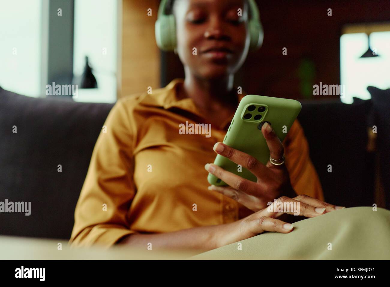 Donna nera con cuffie che naviga sui social media su uno smartphone Foto Stock