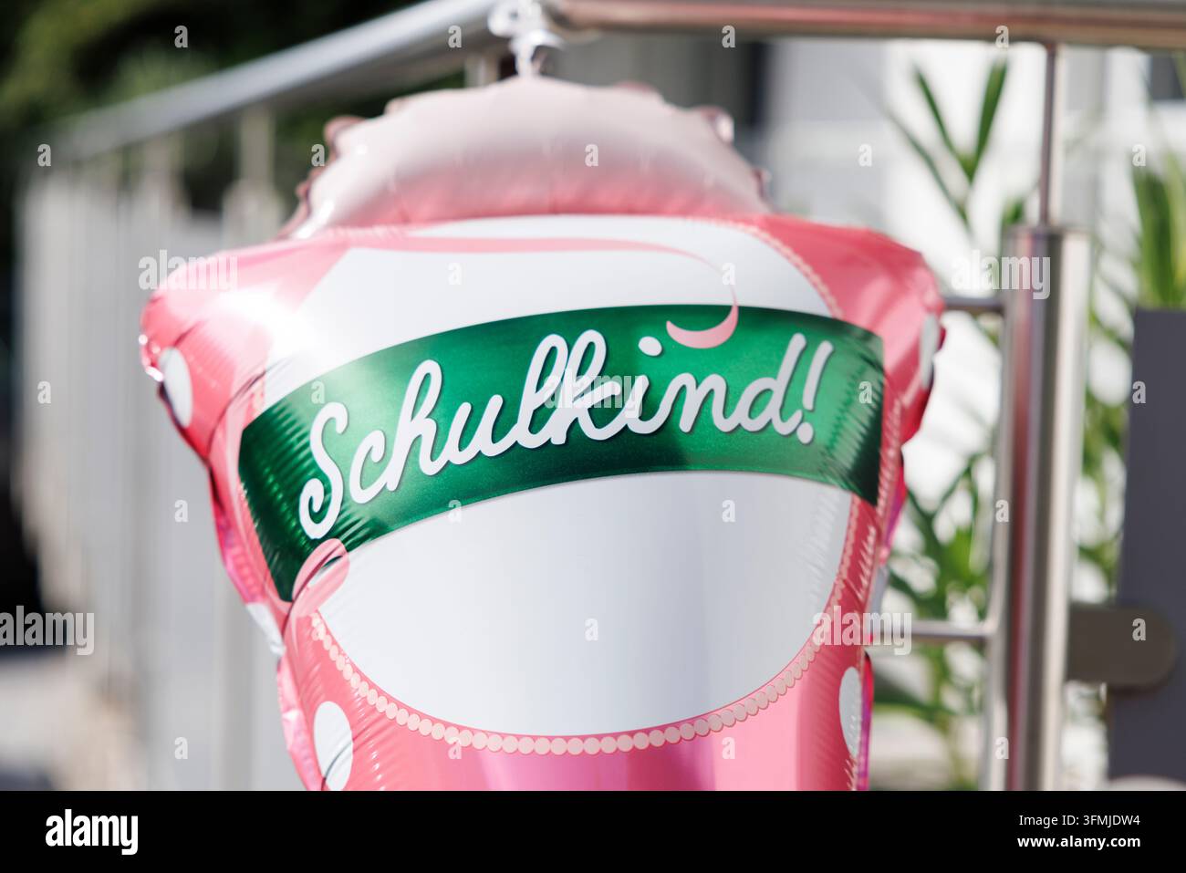 Una grande decorazione di palloncini rosa e bianchi con la scritta „Schulkind!“ è appesa a una ringhiera metallica. Foto Stock