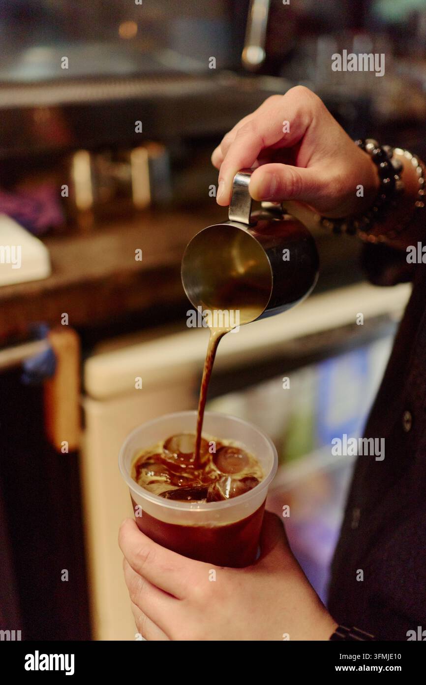 Mani del barista che versano un caffè espresso fresco sul ghiaccio in un bar Foto Stock
