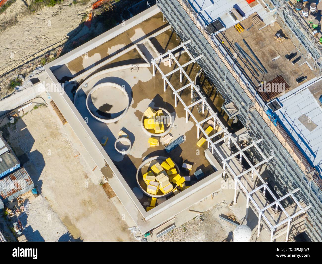 Veduta aerea di un cantiere edile ospedaliero con strutture circolari e materiali isolanti gialli su un tetto piatto con impalcature ad Ancona Foto Stock