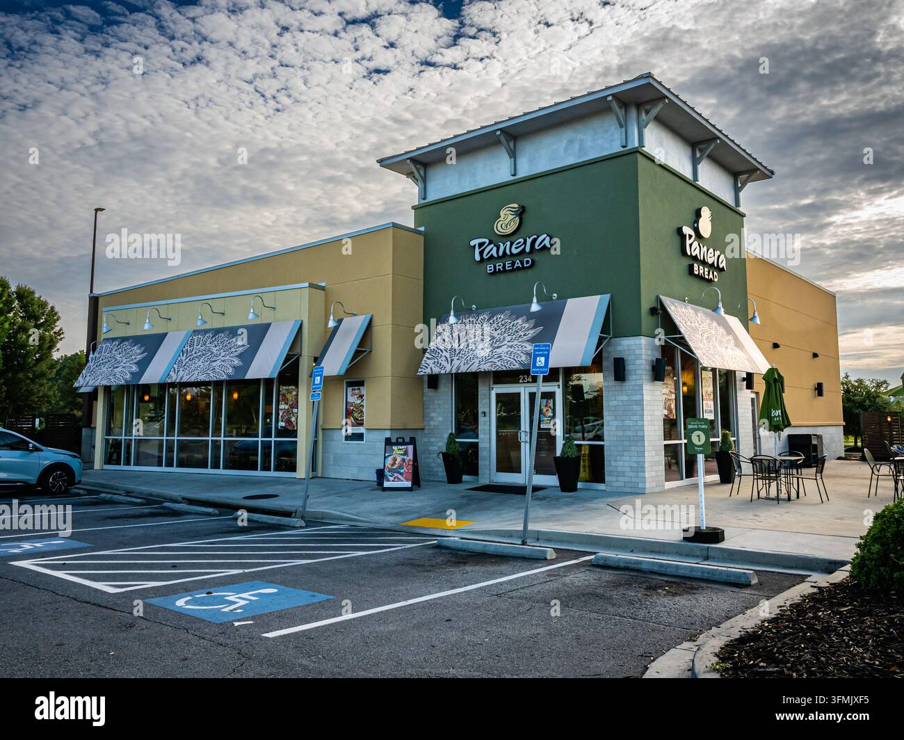 Pooler, Georgia, USA, 5 agosto 2026: Vista esterna di una panetteria-caffè Panera Bread con una facciata angolare verde oliva, loghi Panera Bread color crema e donna Foto Stock