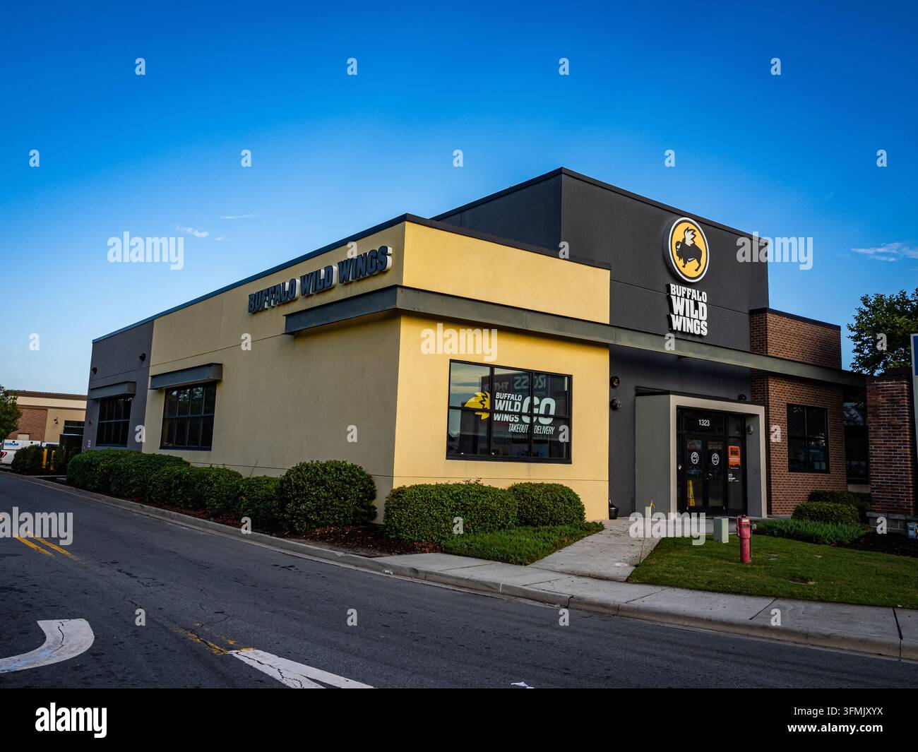 Pooler, Georgia, USA, 5 agosto 2026: Esterno del servizio di consegna a domicilio di Buffalo Wild Wings GO, facciata gialla/antracite, idrante, cespugli ben curati Illus Foto Stock