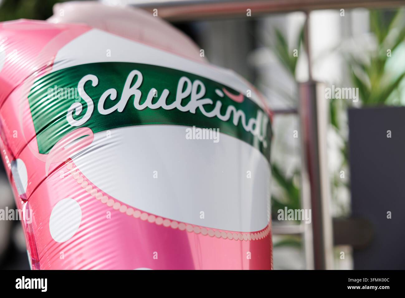 Prima piano di un palloncino di lamina a pois rosa con uno striscione verde "Schulkind!" appeso a una ringhiera metallica. Foto Stock