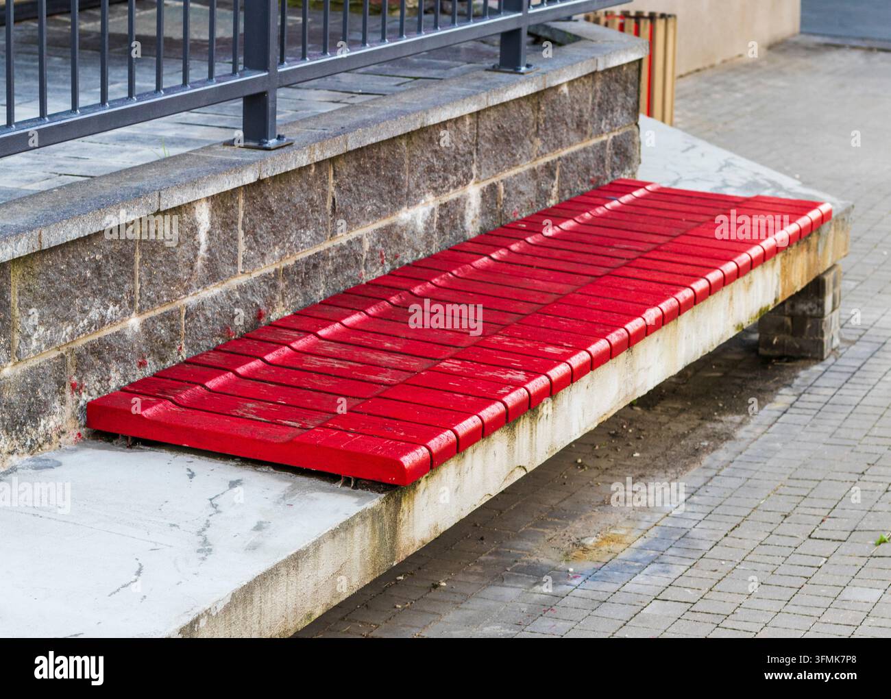 Lunga panca moderna in legno dipinta di rosso su una base in cemento e pietra Foto Stock