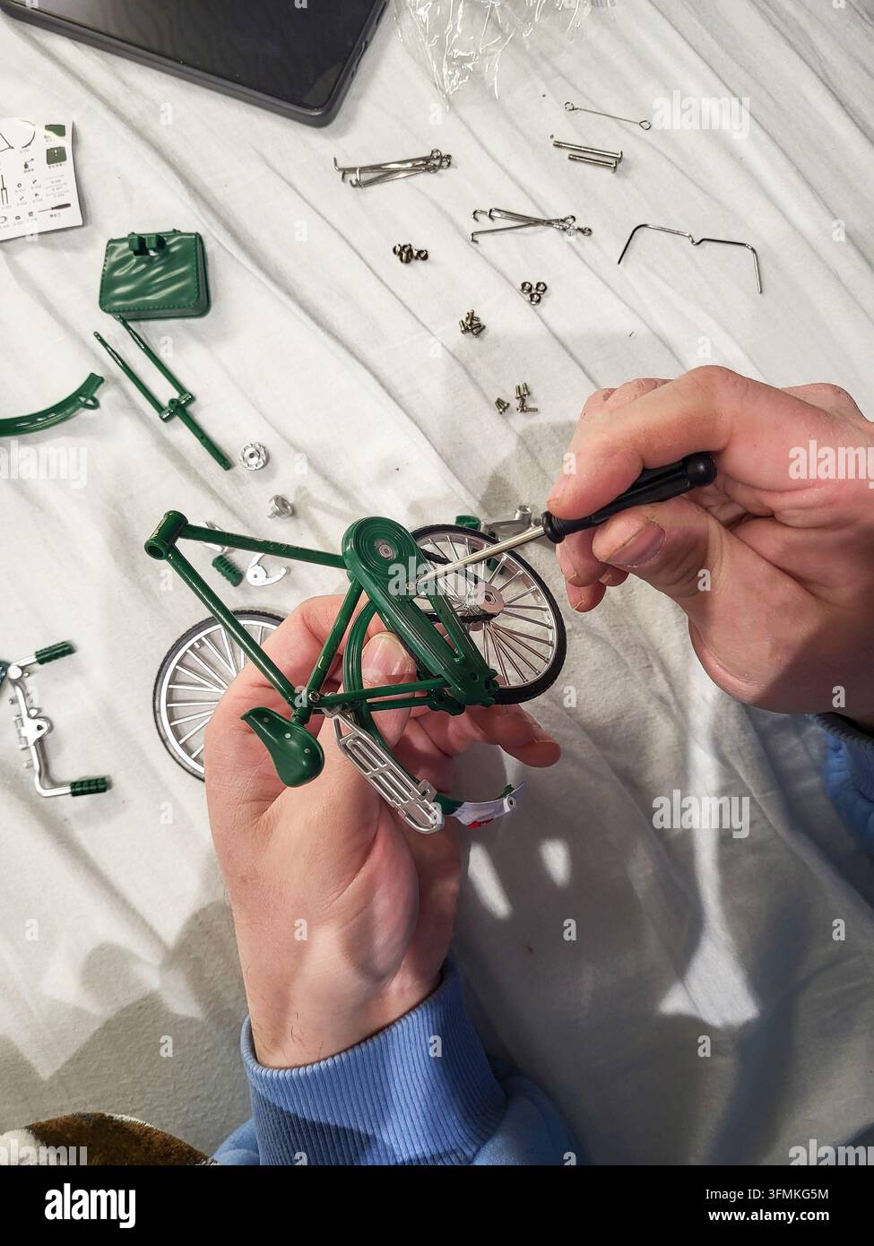 Un uomo che stringe una minuscola vite in un kit di costruzione in metallo in miniatura, primo piano di mani maschili che assemblano il modello con un cacciavite Foto Stock