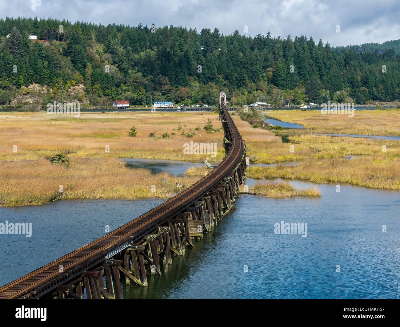 Vista aerea dei binari ferroviari che attraversano una palude e acque libere vicino a Florence, Oregon, evidenziando il percorso ferroviario realizzato dall'uomo attraverso una tranquilla zona umida costiera Foto Stock