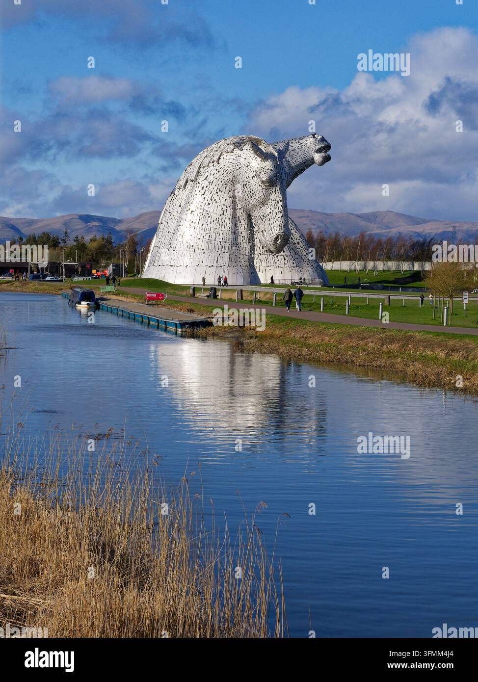 Una vista delle sculture a testa di cavallo alte 30 m di Andy Scott nell'Helix Park, Falkirk, in una giornata di primavera con un canale in primo piano e montagne sullo sfondo. Foto Stock