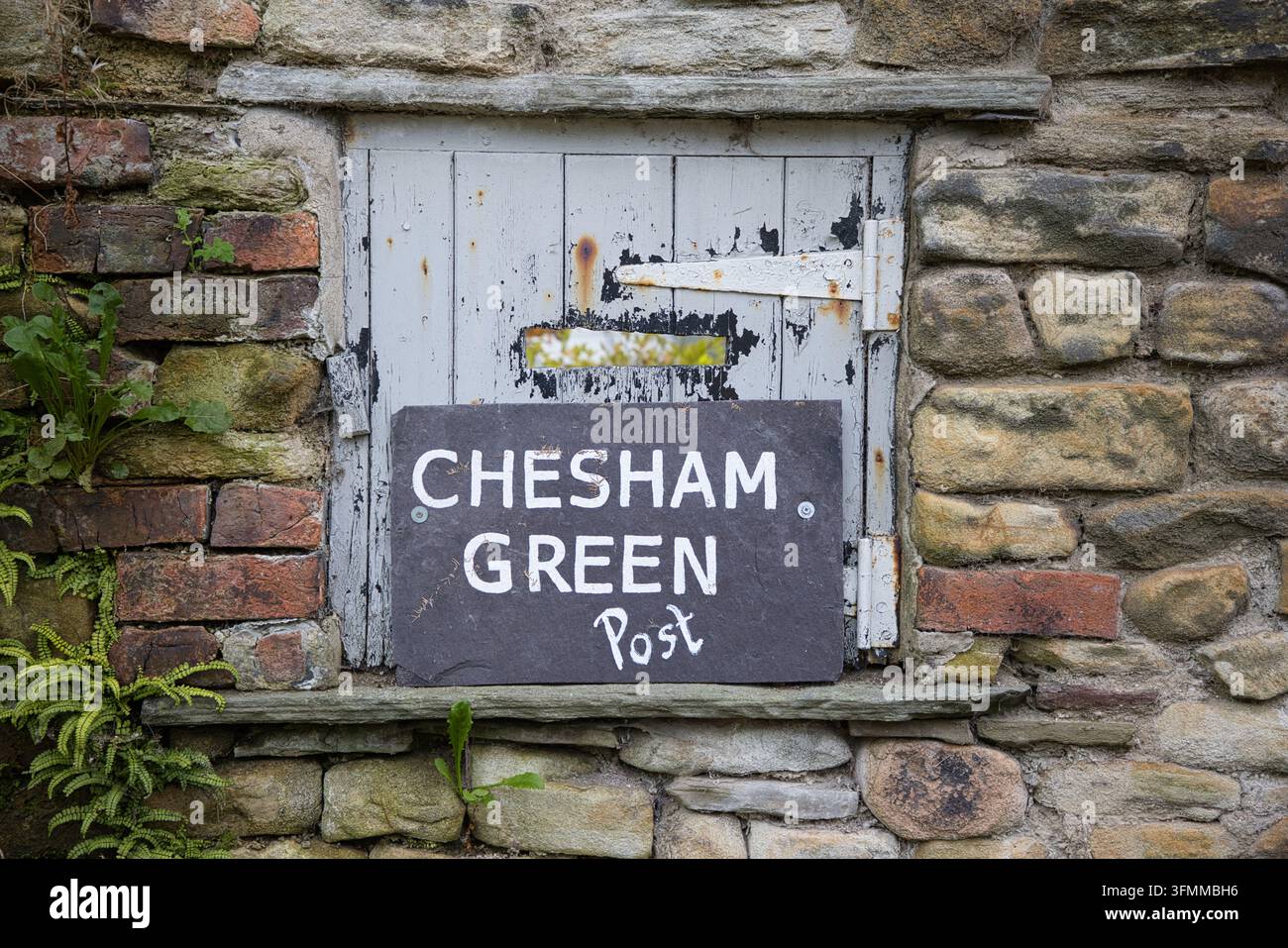Insegna in ardesia scura Chesham Green Post su un muro di pietra davanti a una vecchia porta di legno blu. Foto Stock