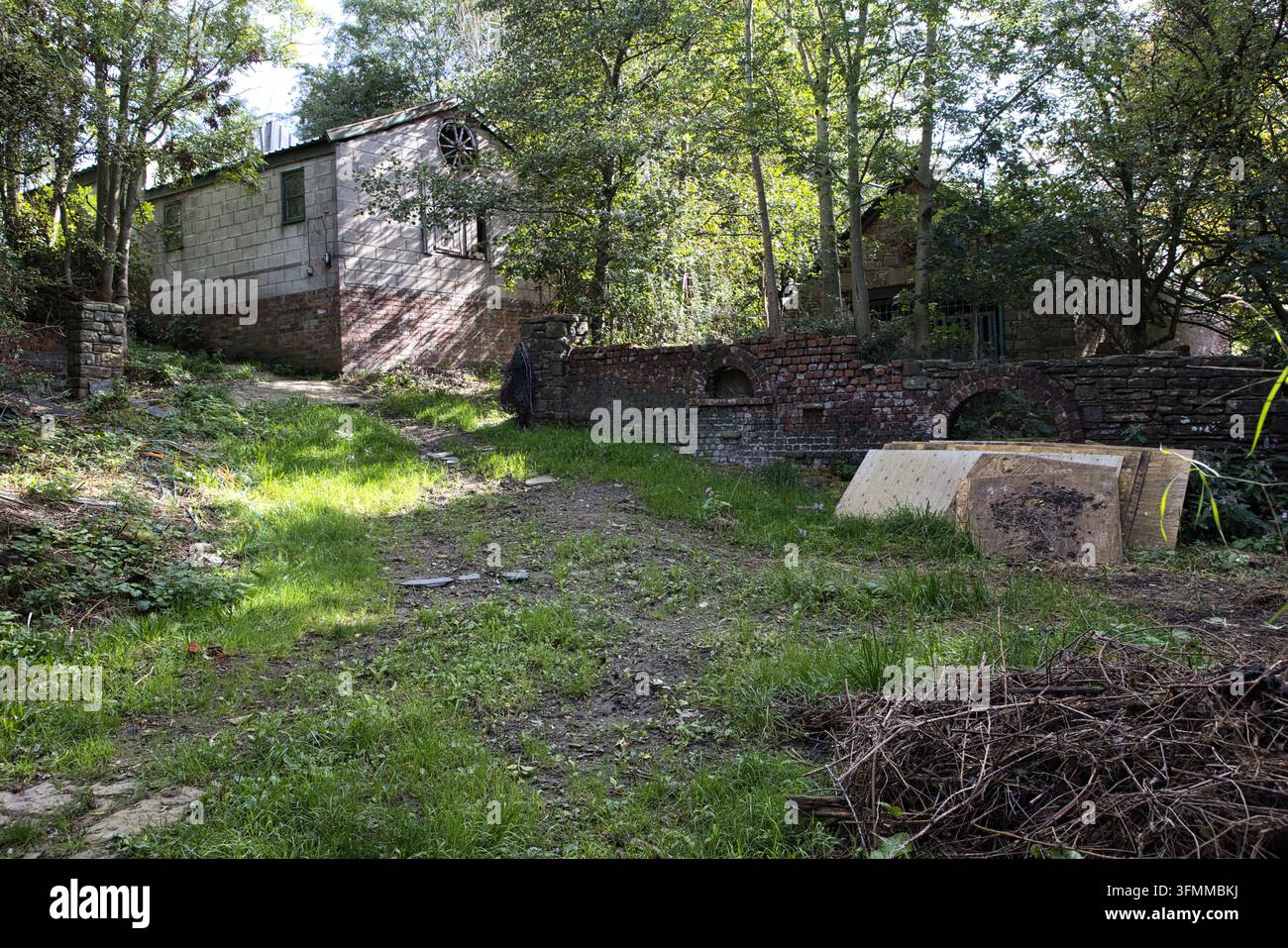 Edificio agricolo rustico in mattoni e pietra con dettagli architettonici e un cortile invaso dalla vegetazione Foto Stock