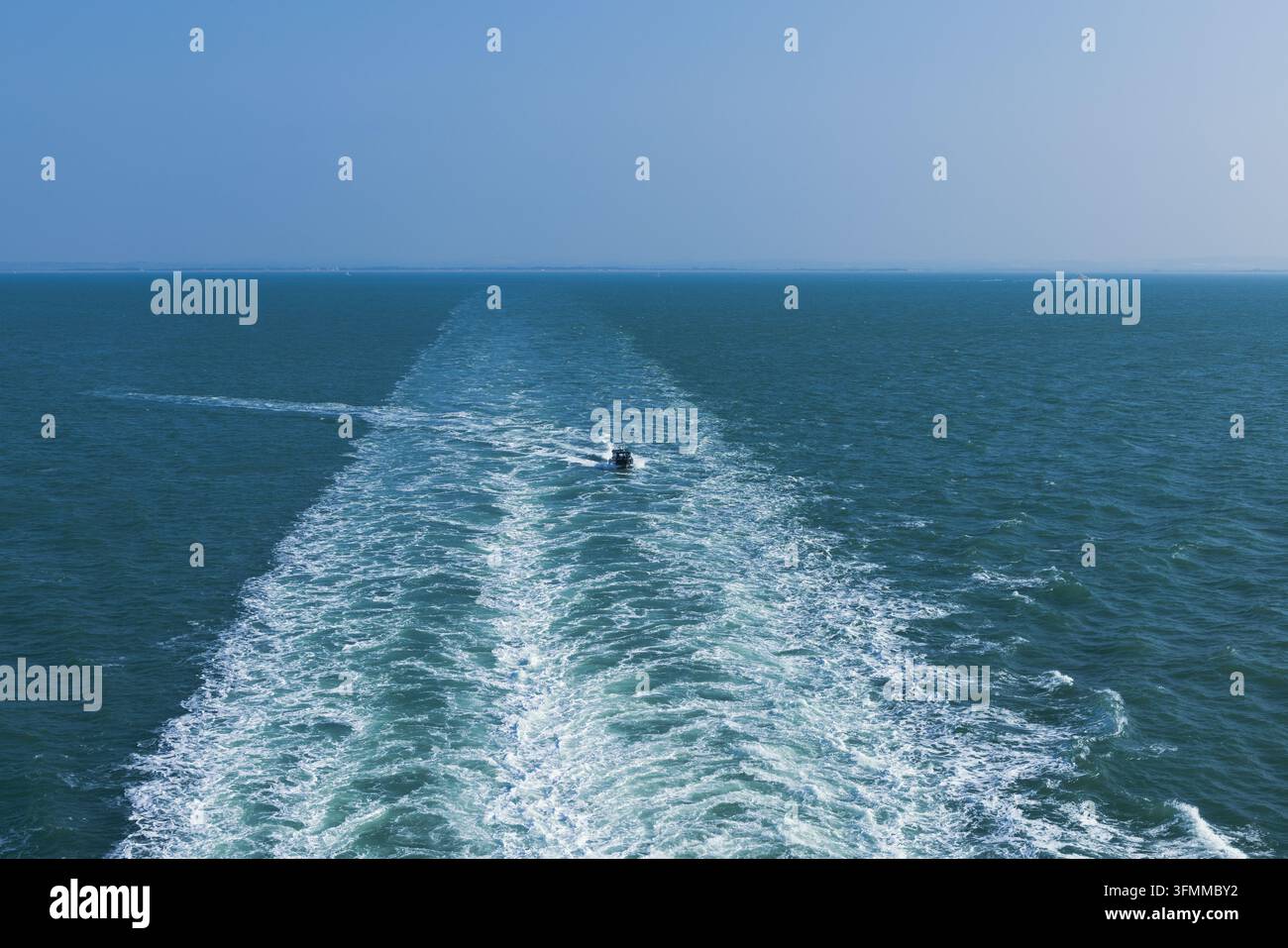 Vista ad angolo alto di una piccola barca che segue il risucchio di una nave molto più grande, tracciando una linea di acqua bianca attraverso il mare aperto, traghetto Portsmouth per la Francia. Foto Stock