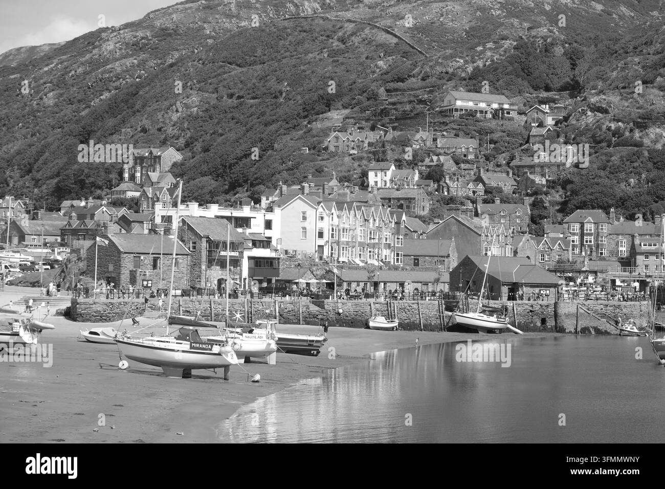 Questa vista monocromatica cattura barche arenate con la bassa marea nel porto di Barmouth, Gwynedd, incastonate contro le colline gallesi nel Galles del Nord Foto Stock