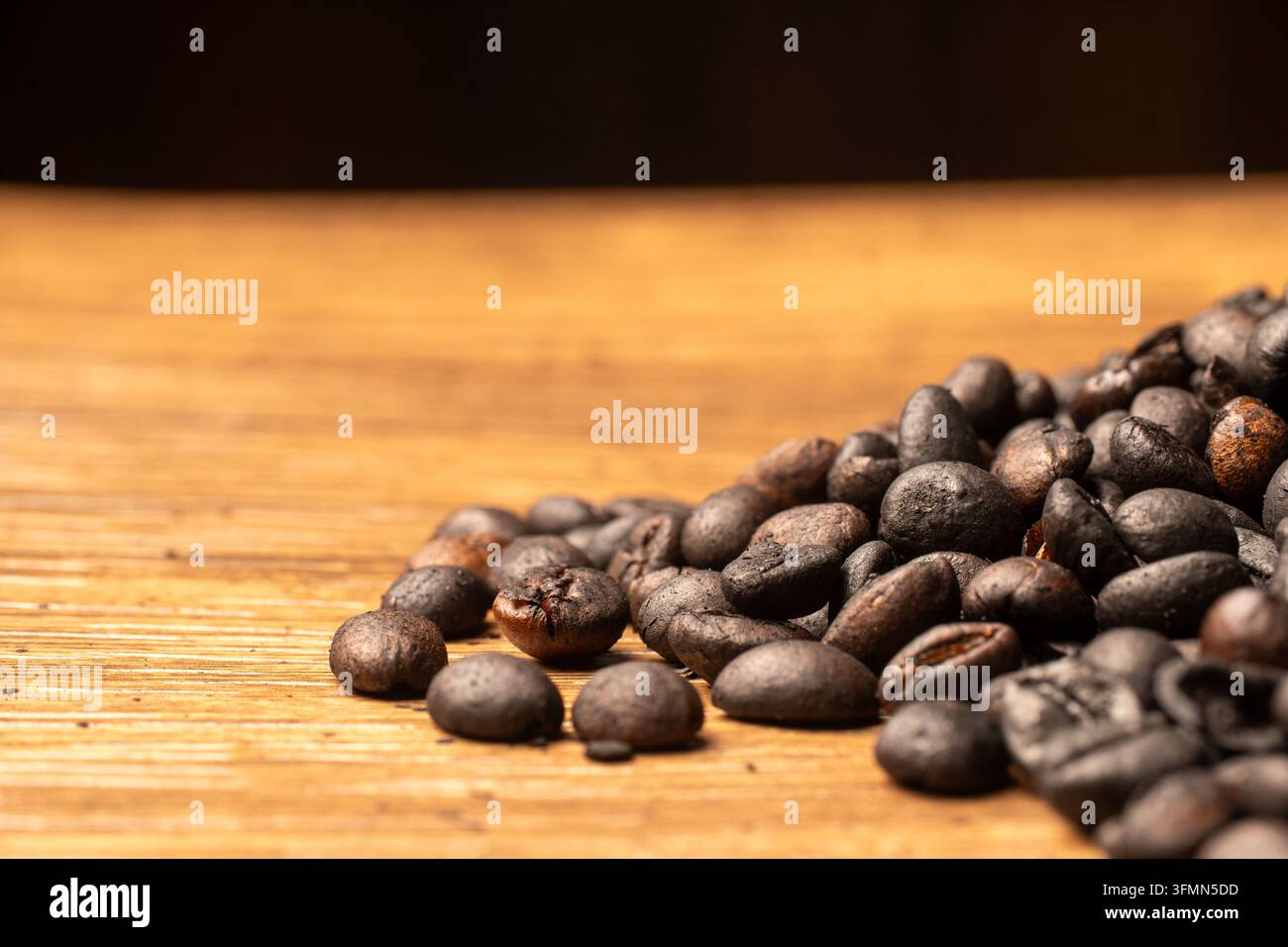 Vista laterale ravvicinata di un mucchio di chicchi di caffè tostati scuri posizionati su una superficie di legno rustico con ampio spazio di copia sfocato sul lato sinistro. Foto Stock