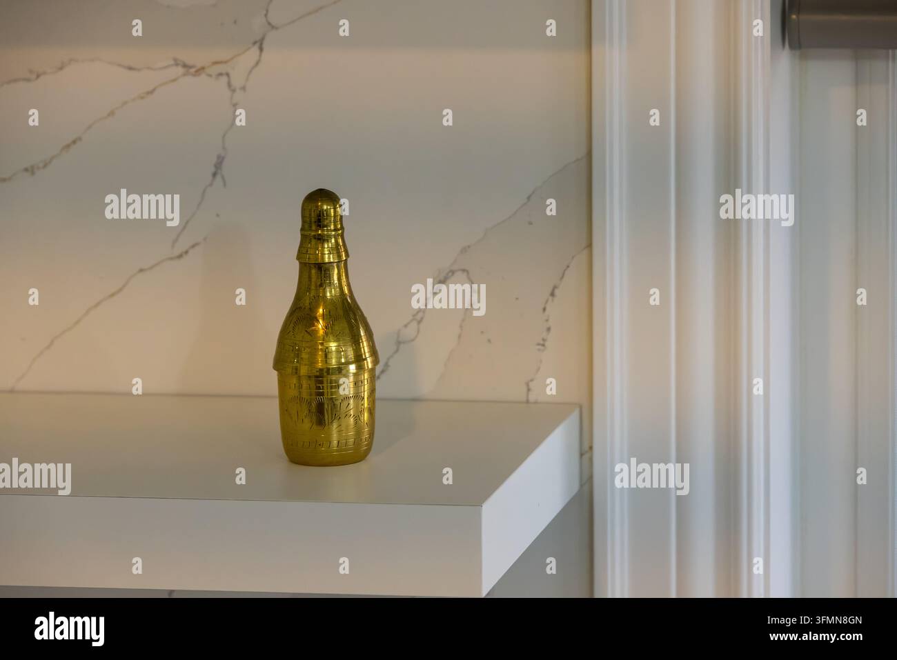 Un ornamento a forma di bottiglia di champagne dorato elegantemente esposto su una superficie di marmo bianco lucido, creando un'atmosfera lussuosa e sofisticata. Ideale per l'uso i Foto Stock