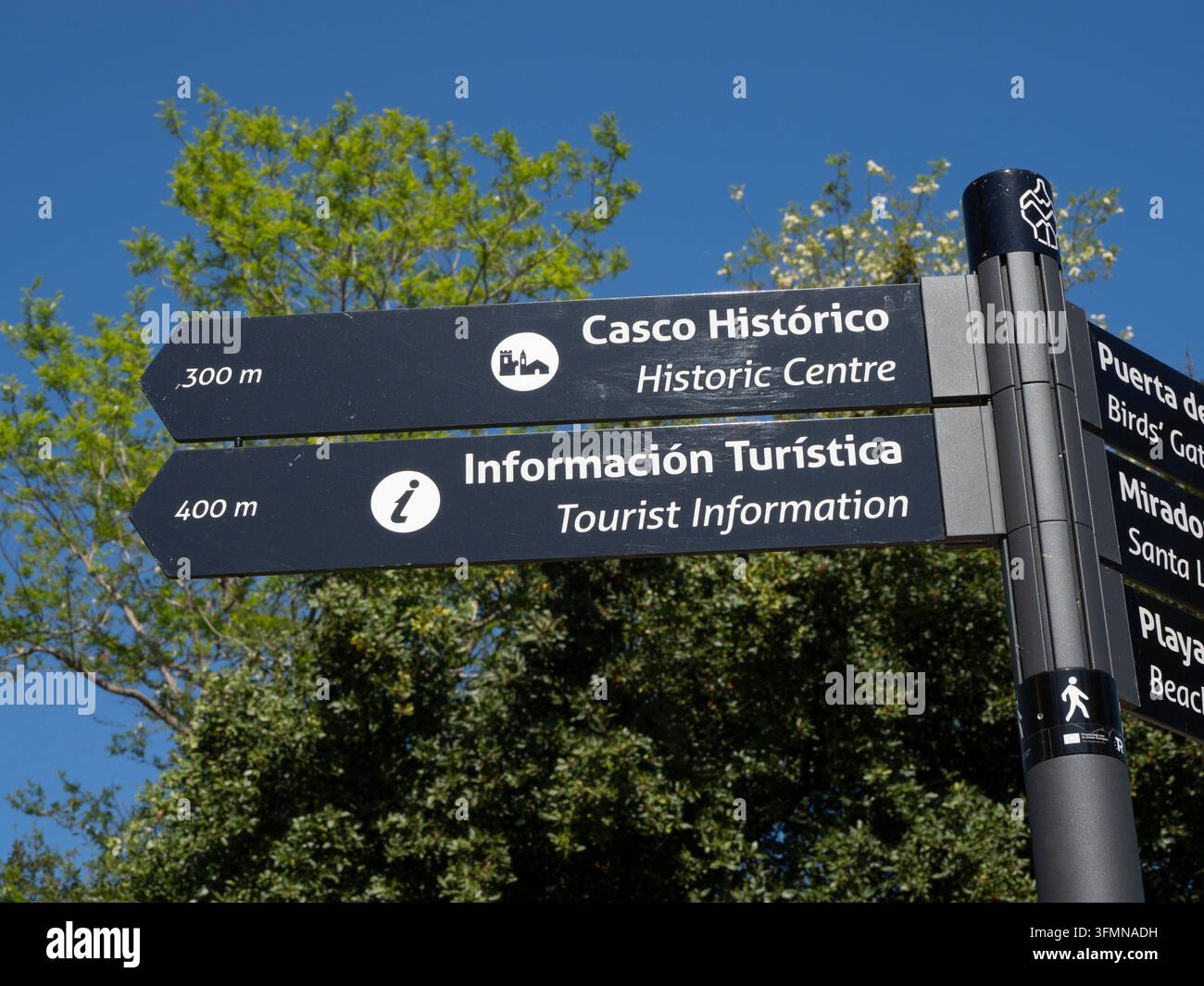 Segnale di informazione turistica spagnolo - Segnali direzionali neri che indicano il centro storico, la spiaggia e l'informazione turistica sotto un cielo blu con g Foto Stock