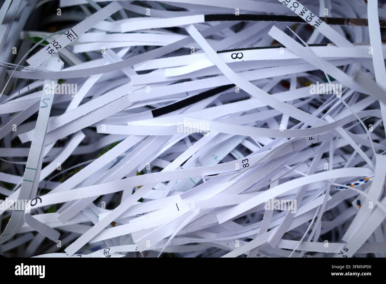 Strisce sottili di carta bianca sminuzzata sono intrecciate in un mucchio caotico. Ogni striscia presenta testo e numeri stampati, suggerendo che provengano da documenti. Th Foto Stock