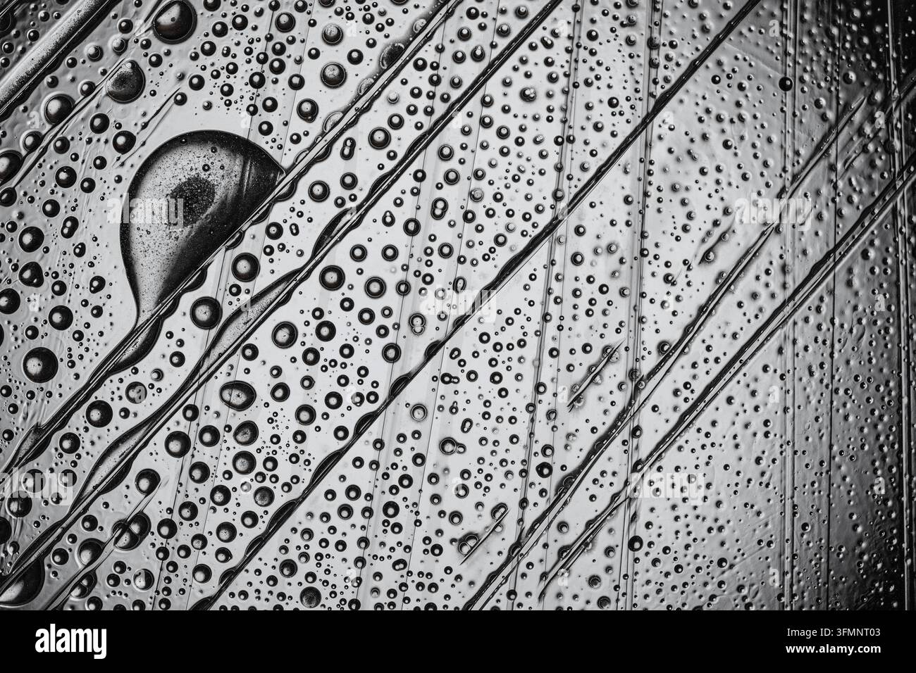Gocce d'acqua che formano un motivo astratto su una superficie strutturata, con dimensioni variabili delle gocce e linee diagonali marcate Foto Stock
