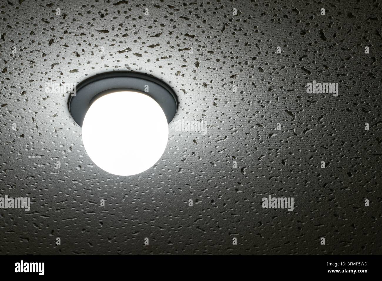 Lampadina luminosa su superficie ruvida di cemento in spazio interno buio Foto Stock