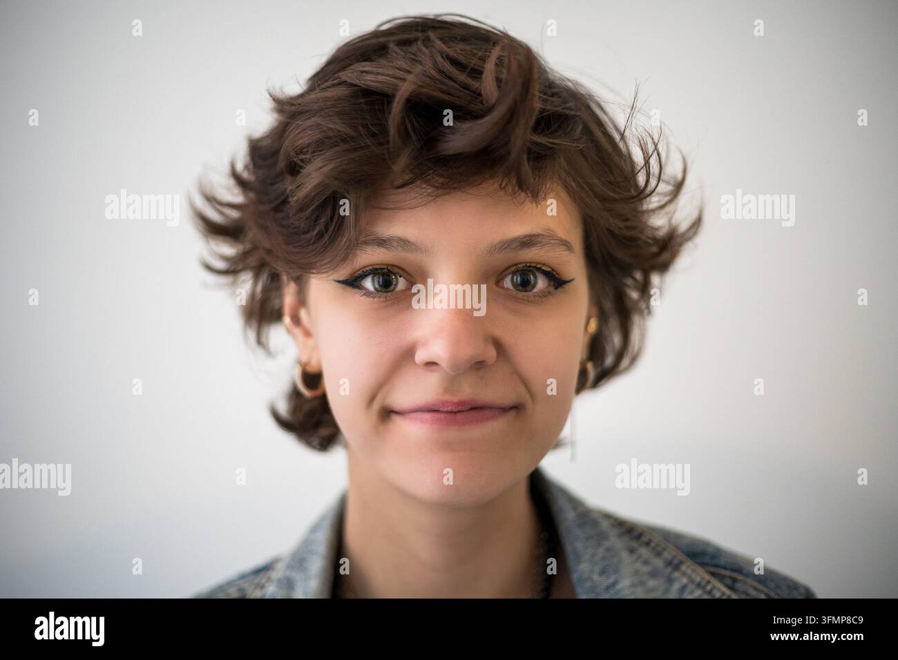 Ritratto di una giovane donna con sguardo diretto e sorriso sottile che trasmette sicurezza, autenticità, individualità, cordialità, apertura e stile contemporaneo. Foto Stock