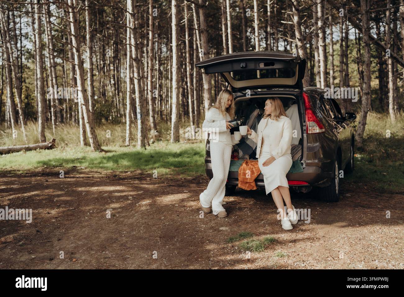 Madre e figlia che godono di una pausa nella foresta in auto, simboleggiando uno stile di vita di mobilità dolce, la cultura della terapia forestale e il legame intergenerazionale nel vivere lento Foto Stock