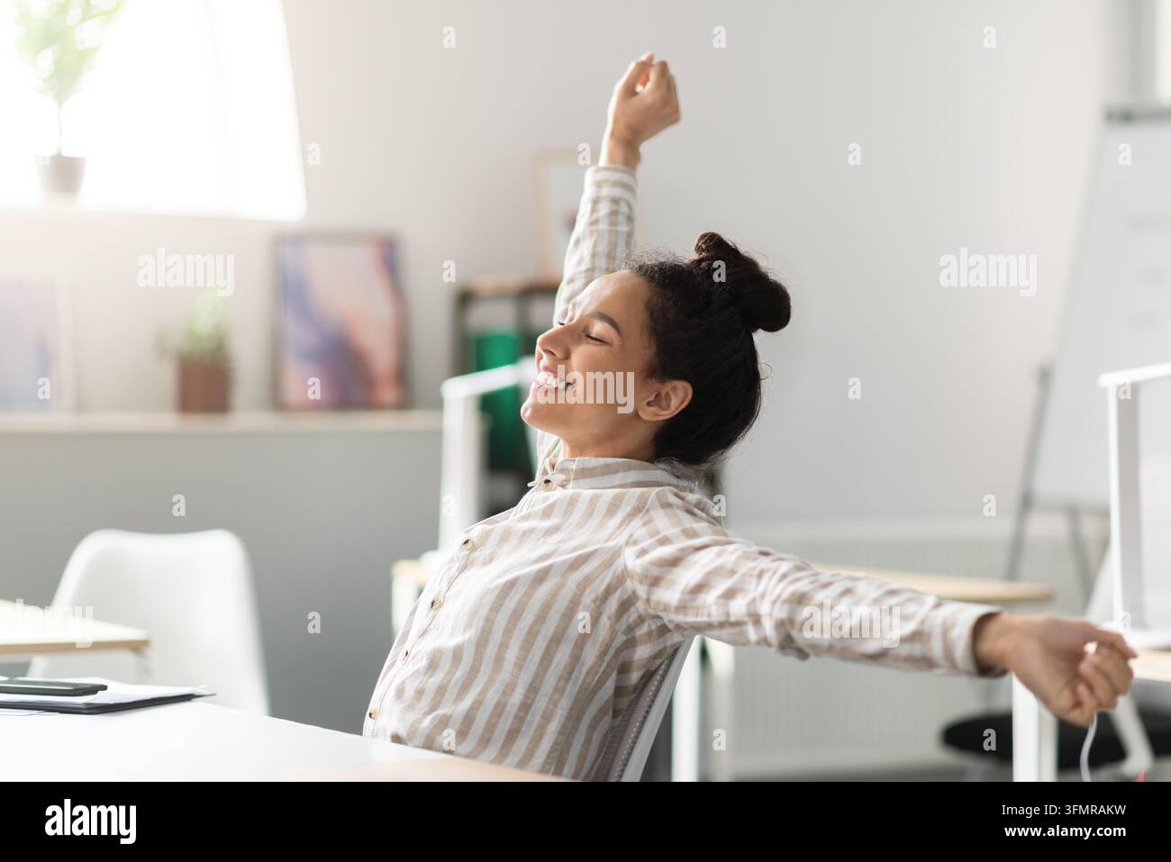 Giovane donna felice che si allunga alla scrivania in ufficio, si sente rilassata e allegra, concetto di benessere Foto Stock