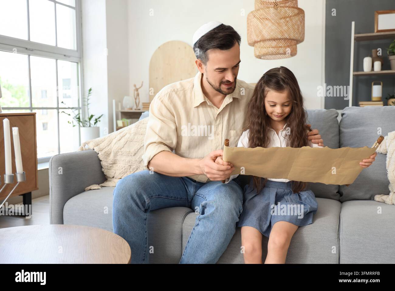 Educazione ebraica e tradizione familiare, padre e figlia leggono insieme un rotolo della Torah a casa per lo studio religioso e la connessione al patrimonio culturale Foto Stock